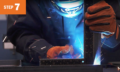 Operator tack welds while holding a table leg.
