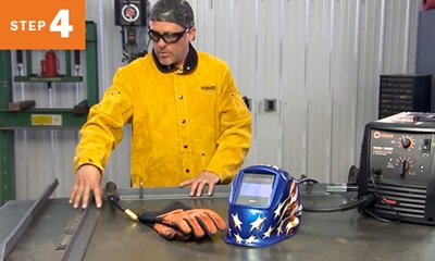 welder standing in front of a table with metal and welding equipment